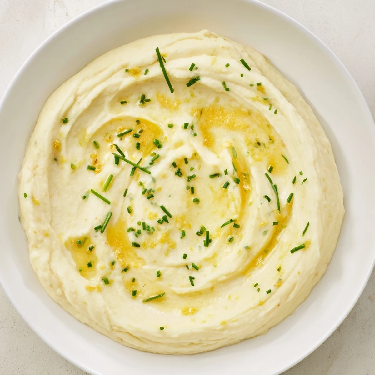 A bowl of creamy Roasted Garlic Mashed Cauliflower, smelling of roasted garlic and fresh herbs.