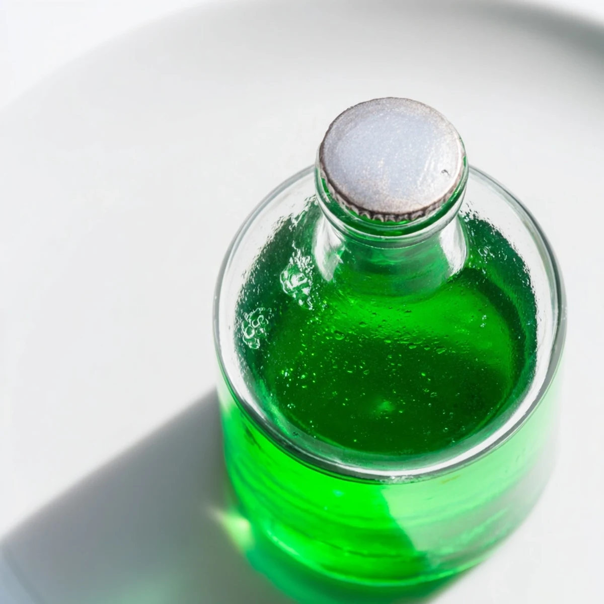 Pouring a refreshing, bright green Peppermint Cordial into a glass with ice cubes.