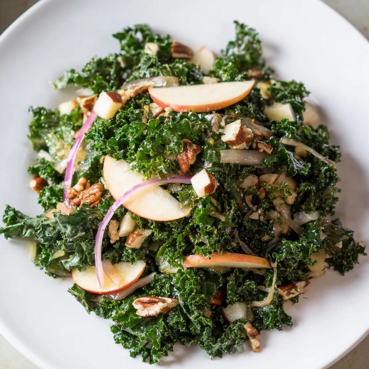 Bright bowl of Winter Kale Salad with Apple and Sharp Cheddar topped with shaved cheese and red onion on a marble counter. 
