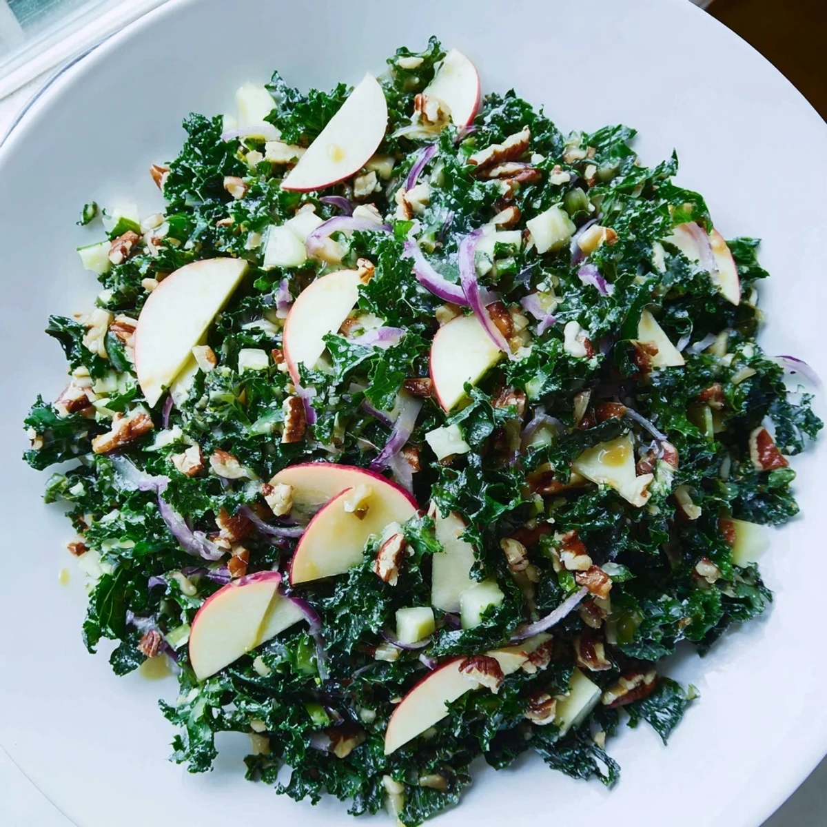 A close-up of vibrant Winter Kale Salad with Apple and Sharp Cheddar featuring massaged greens, sweet apple wedges, and crunchy nuts.