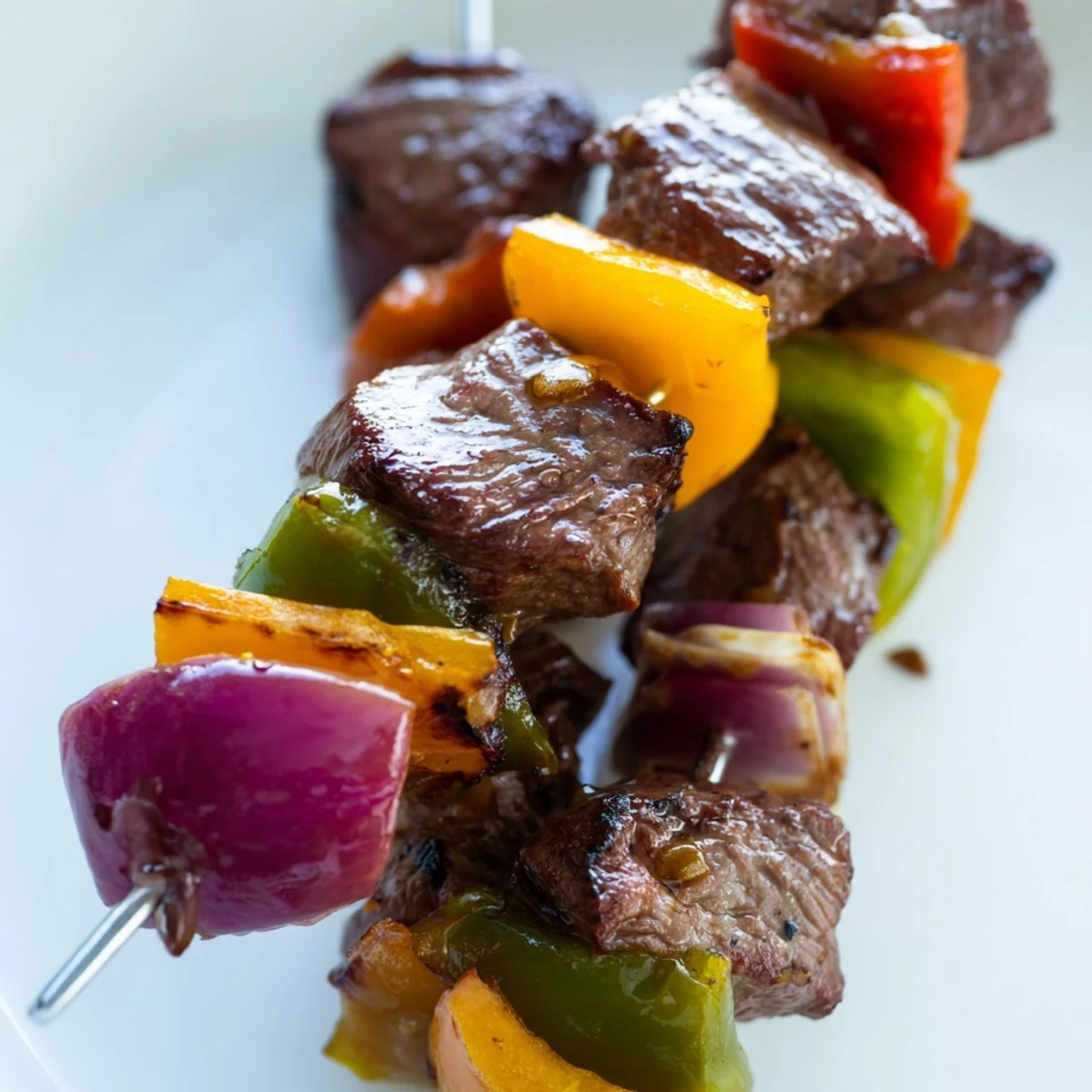 Sizzling grilled Beef Kebabs with Bell Peppers and Red Onion are stacked on a platter, showcasing juicy seared beef and tender, charred vegetables.