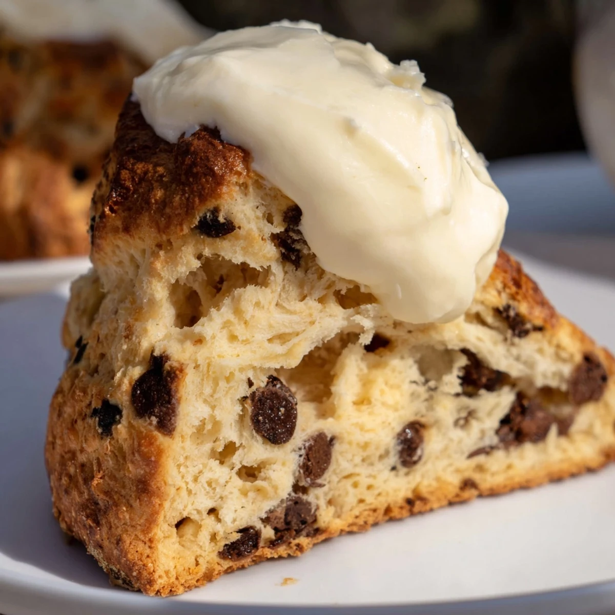 Golden-brown Chocolate Chip Scones with Clotted Cream sit on a rustic wooden board, ready to be split open.