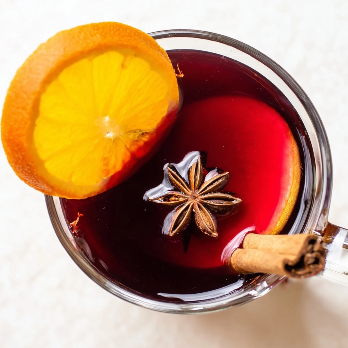 Clear glass mug filled with warm Spiced Alcohol-Free Wine, garnished with star anise, cloves, and fresh orange wheels.