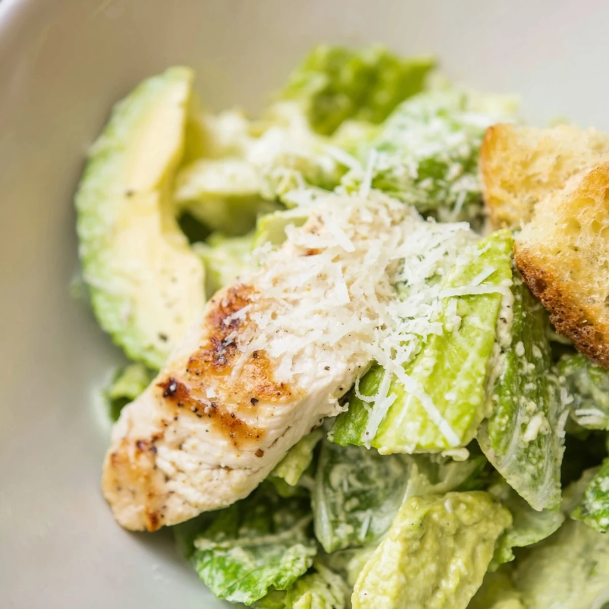 A top-down view of a vibrant Chicken Caesar Salad with Avocado, showcasing juicy grilled chicken slices, creamy avocado, and crisp romaine on a rustic wooden table.