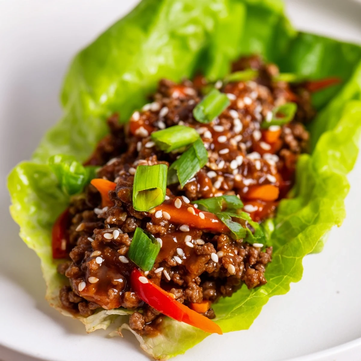 Freshly cooked ground beef with diced vegetables tossed in glossy hoisin sauce, spooned into crisp green lettuce cups, ready to eat.