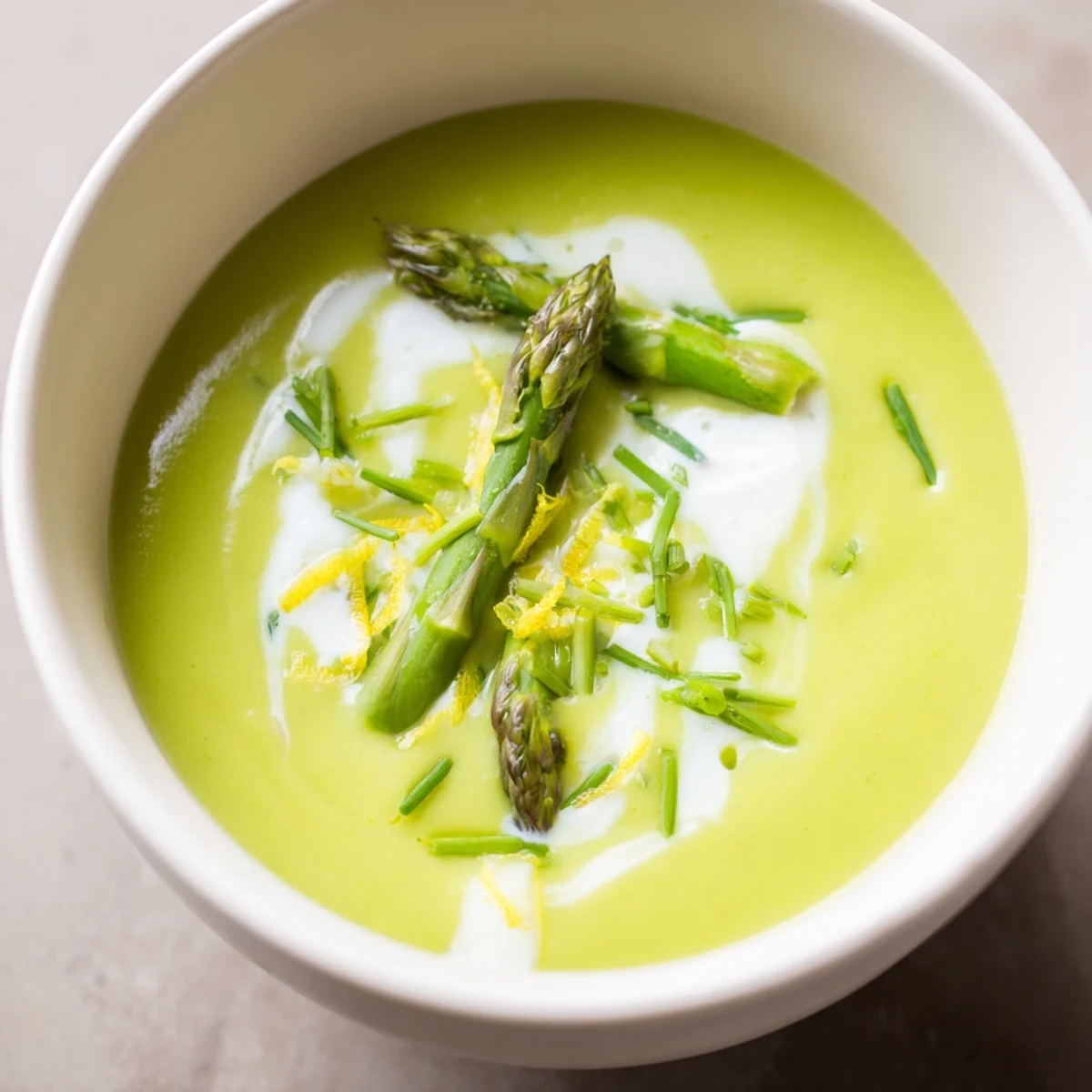Vibrant green Creamy Asparagus Soup with Lemon topped with chives, ready to enjoy in a cozy kitchen.