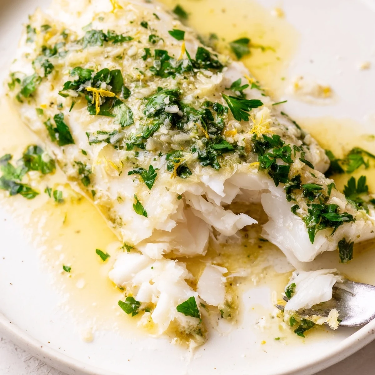 Golden Baked Halibut with Garlic and Lemon Butter is presented on a white plate, garnished with fresh parsley and lemon wedges.