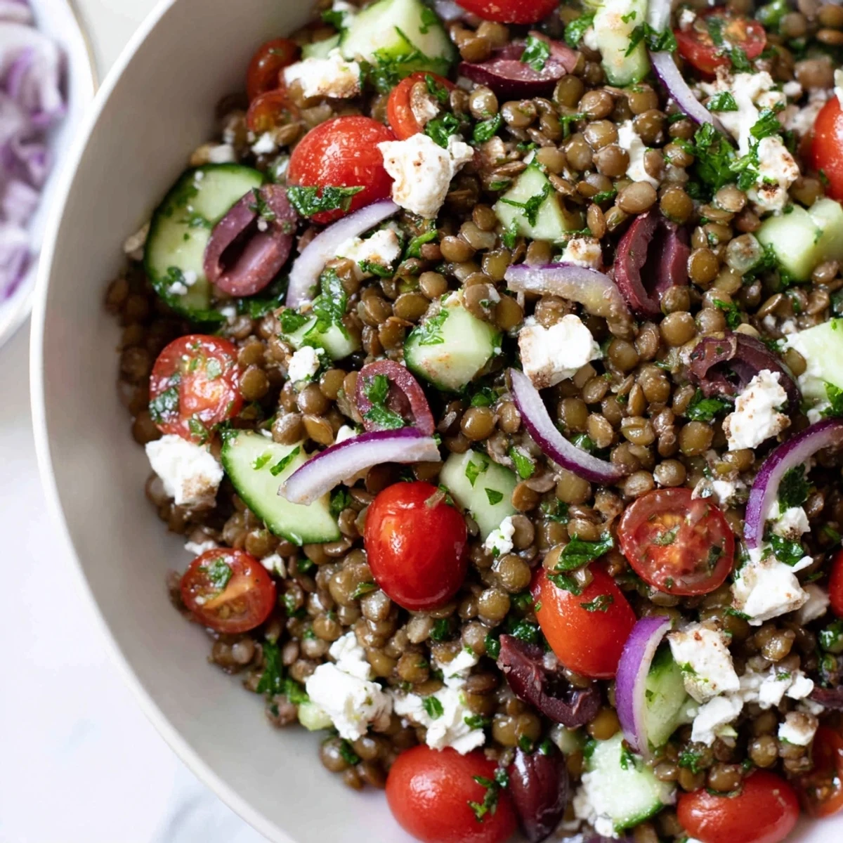 Colorful Mediterranean Lentil Salad topped with sliced Kalamata olives, diced roasted red peppers, and chopped parsley served in a white ceramic bowl.