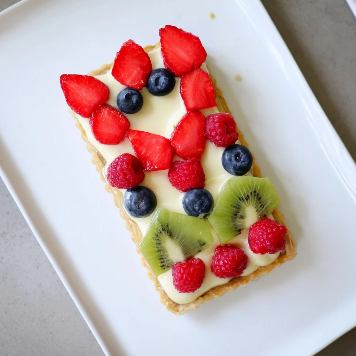 Golden-brown Love Letter Fruit Tart on a marble board, with silky vanilla cream and fresh strawberries, raspberries, and blueberries arranged as an envelope.