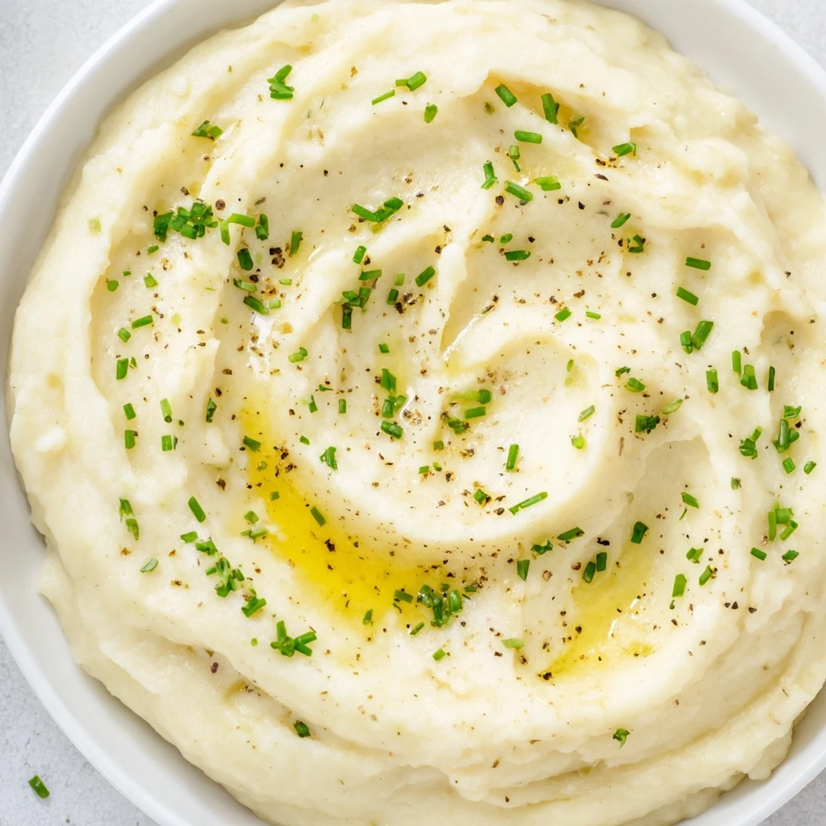 Roasted garlic mashed cauliflower served warm as a gluten-free alternative to potatoes, topped with fresh green chives.