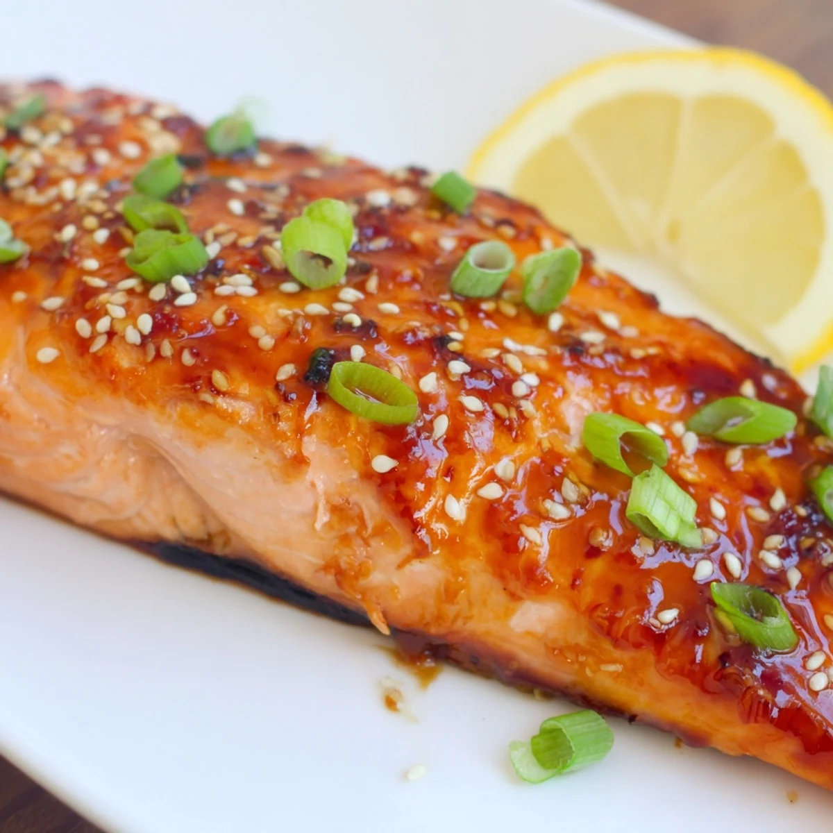A close-up of tender, flaky baked salmon drizzled with sweet and savory teriyaki glaze, served with lemon wedges for a complete meal.