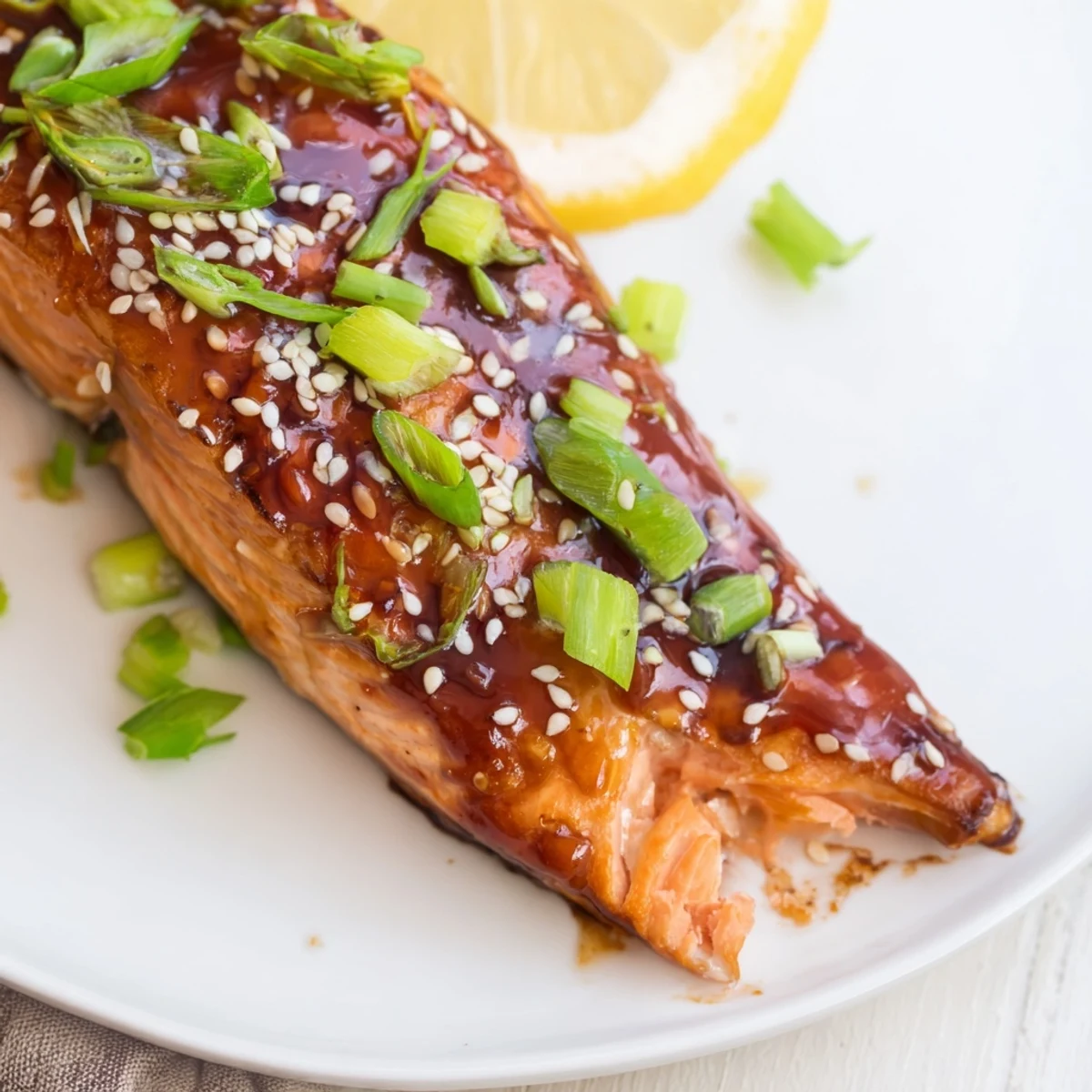 Glossy baked salmon fillets coated in a homemade teriyaki glaze, garnished with fresh green onions and sesame seeds on a baking sheet.