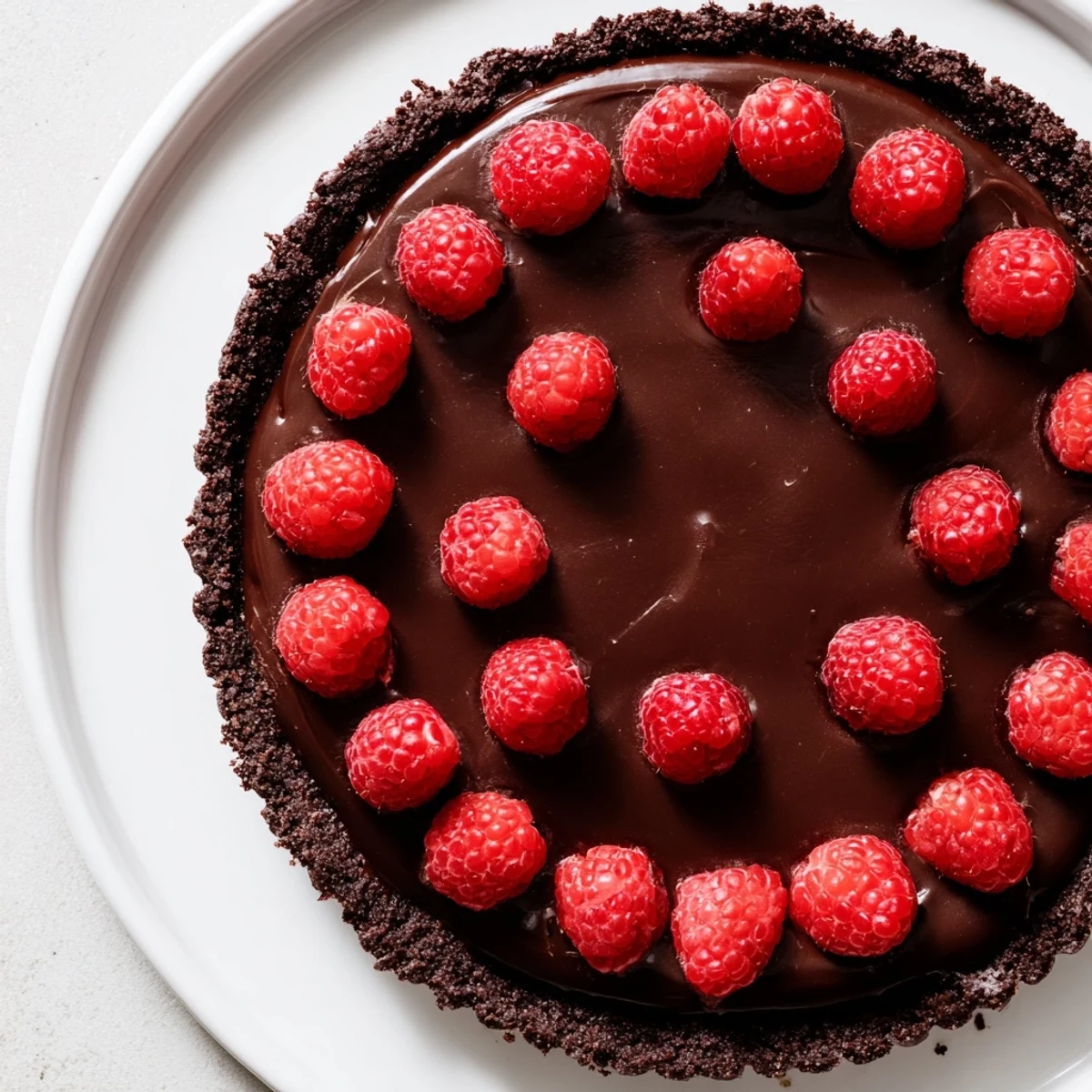 Fresh raspberries artfully arranged on a glossy dark chocolate ganache filling in a Chocolate Raspberry Tart with Ganache.