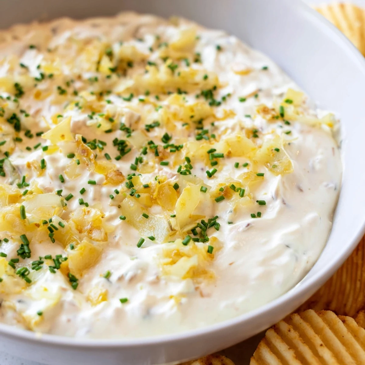 Creamy Game Day Onion Dip with Potato Chips sits in a rustic bowl, garnished with fresh chives, ready for a party platter.