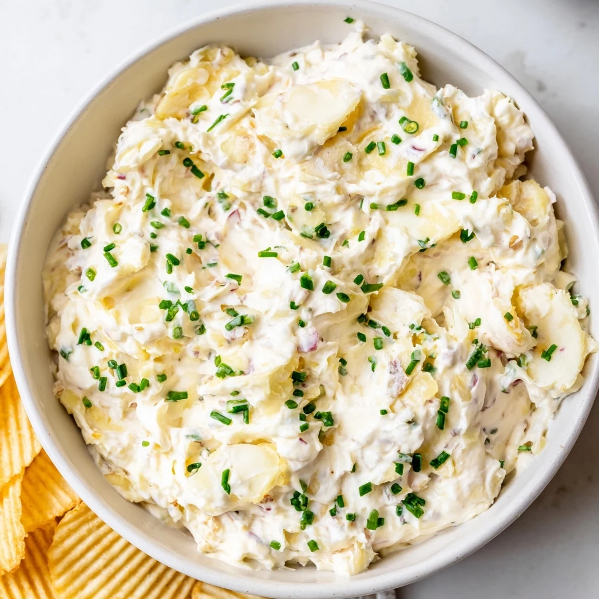 Golden, caramelized onion dip topped with chopped chives and parsley beside a heaping pile of sturdy, crunchy potato chips.