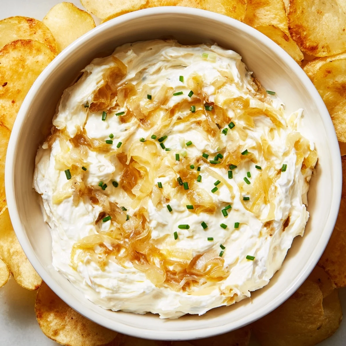 Creamy homemade onion dip in a ceramic bowl, surrounded by crispy potato chips for dipping at a party.