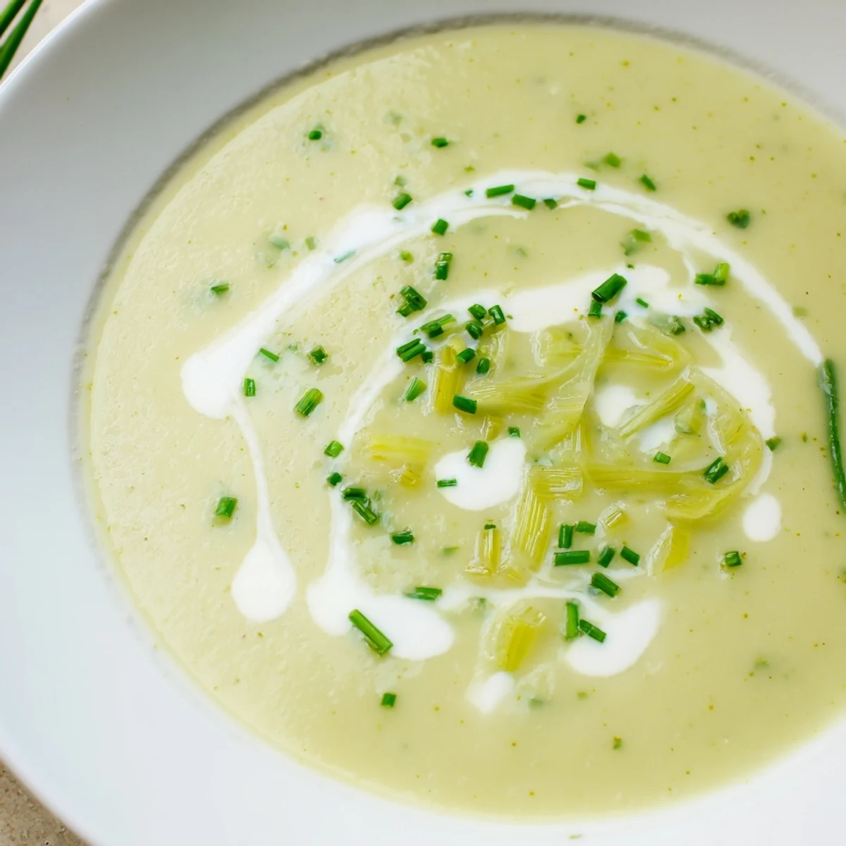 Silky smooth leek and potato soup with cream garnished with fresh chives and a swirl of cream in a rustic bowl.  