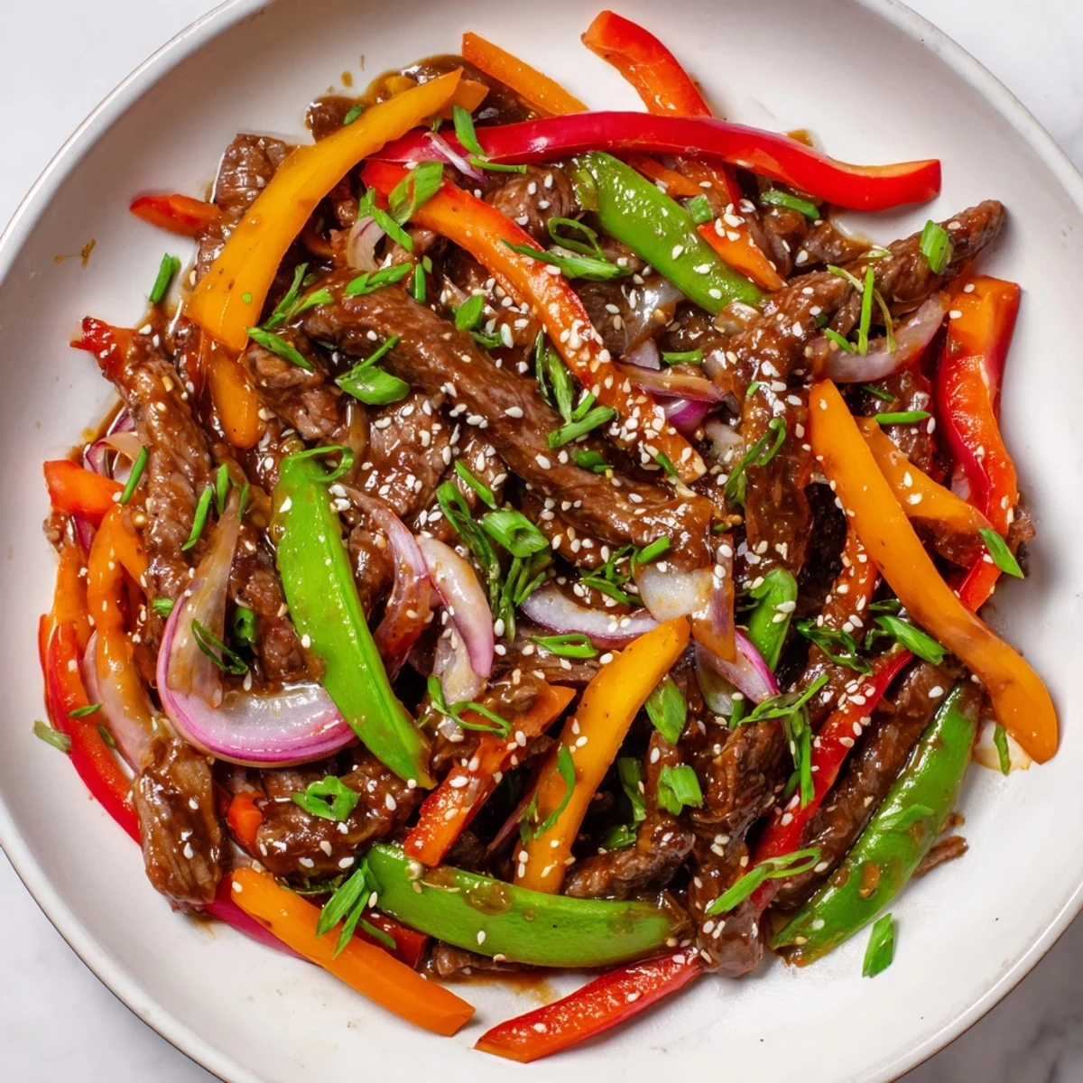 Vibrant red and yellow vegetables tossed with spicy beef stir fry, glistening with sauce and topped with fresh green onions.