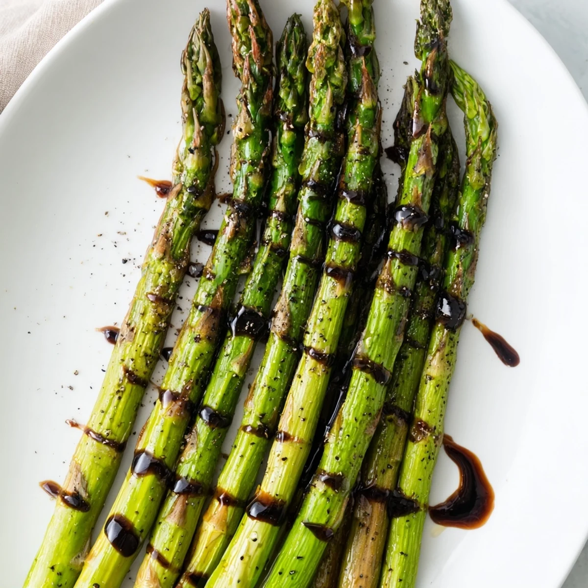 Tender roasted asparagus spears with balsamic glaze on a white platter, garnished with black pepper.  