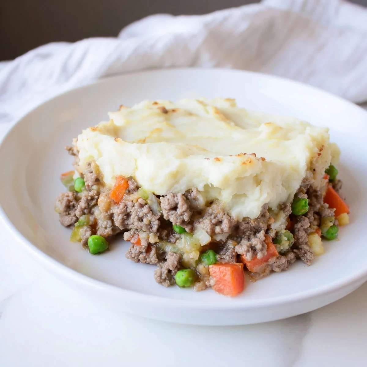 Serving dish of Beef Shepherds Pie with Cauliflower Mash, creamy white topping beside a fresh green salad.