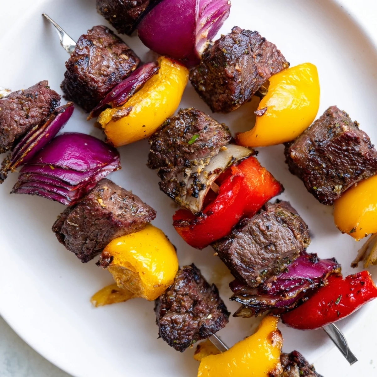 Grilled Beef Kebabs with Bell Peppers and Onions sizzling on a barbecue with char marks and colorful vegetables.