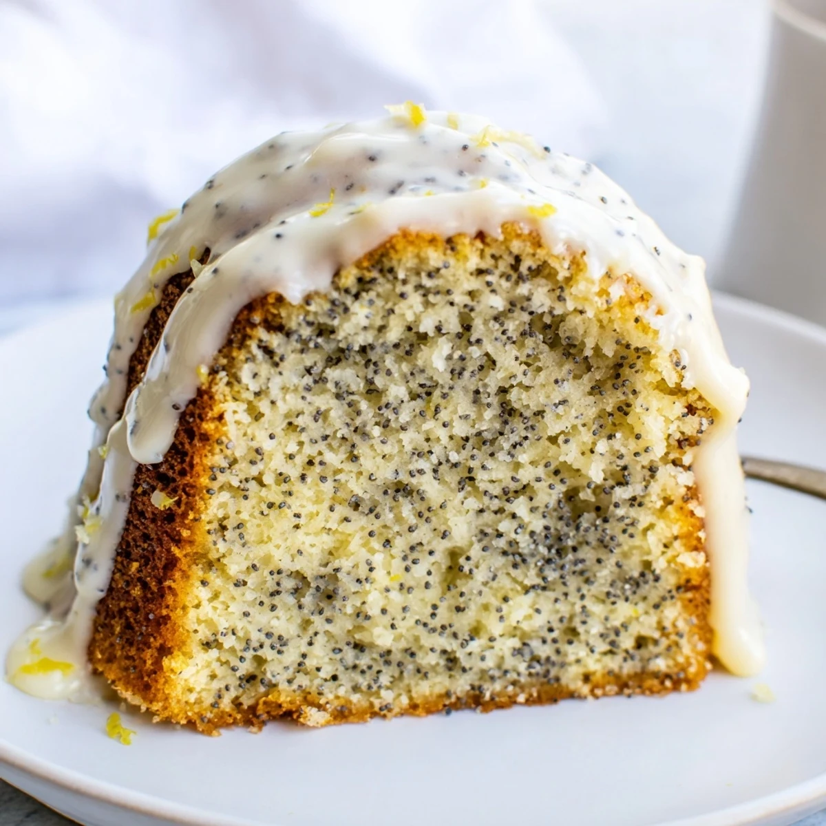 Golden Lemon Poppy Seed Bundt Cake with glossy icing on a marble countertop, sliced to reveal moist crumb with poppy seeds.