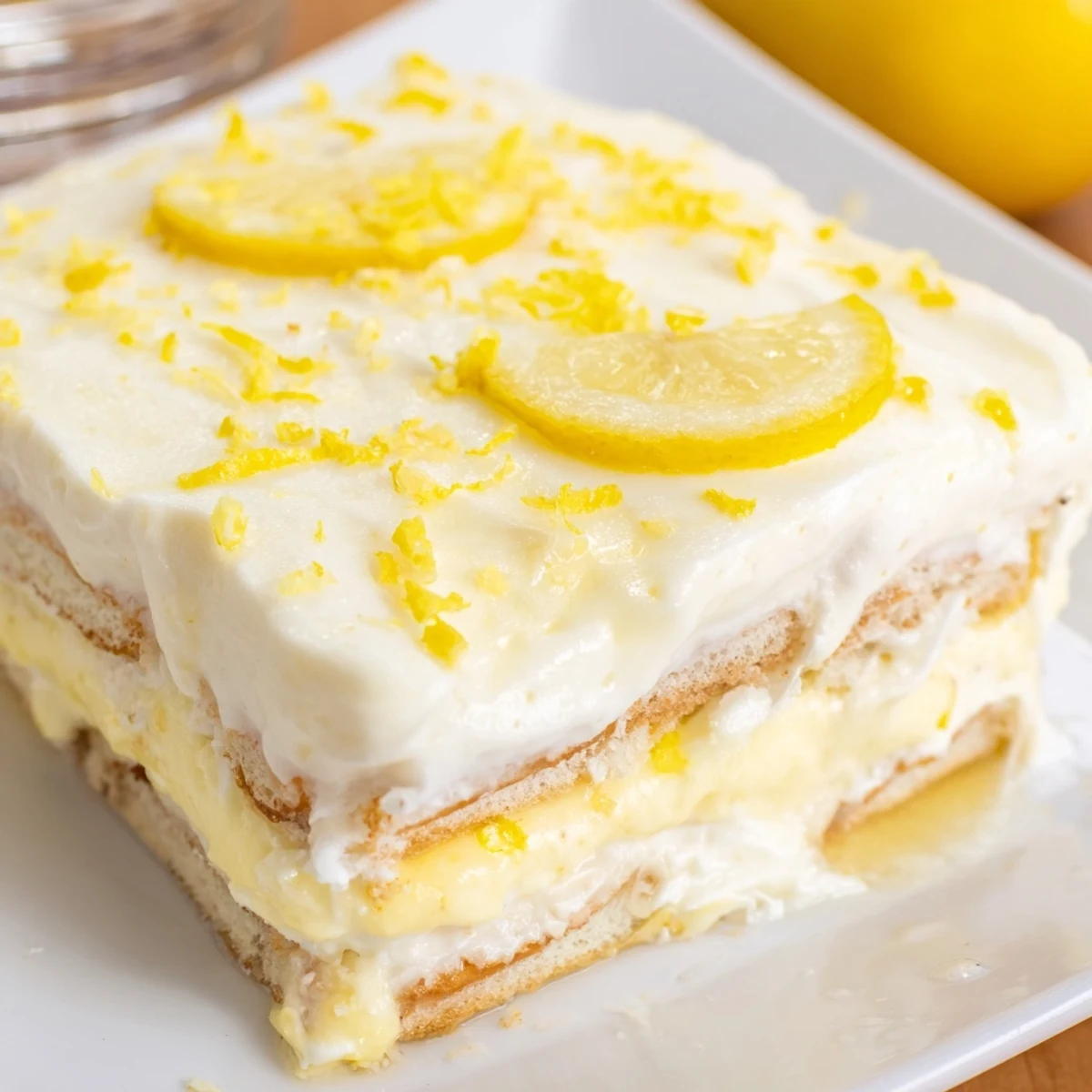 The Easy Lemon Tiramisu No Bake Dessert shows creamy layers in a white dish garnished with fresh lemon slices.