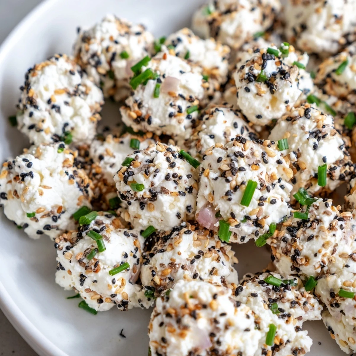 Stack of gluten-free Everything Bagel Cottage Cheese Bites with red onion bits and sesame seeds on a marble counter.