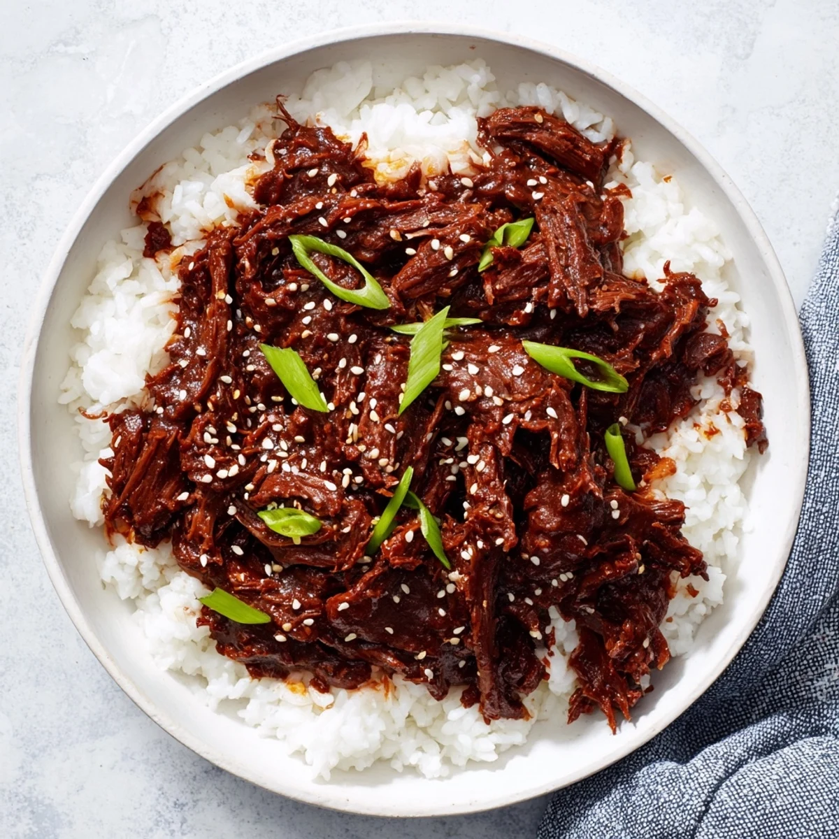 A close-up of tender shredded Crock Pot Korean Beef piled high on fluffy jasmine rice, garnished with sliced green onions and toasted sesame seeds.