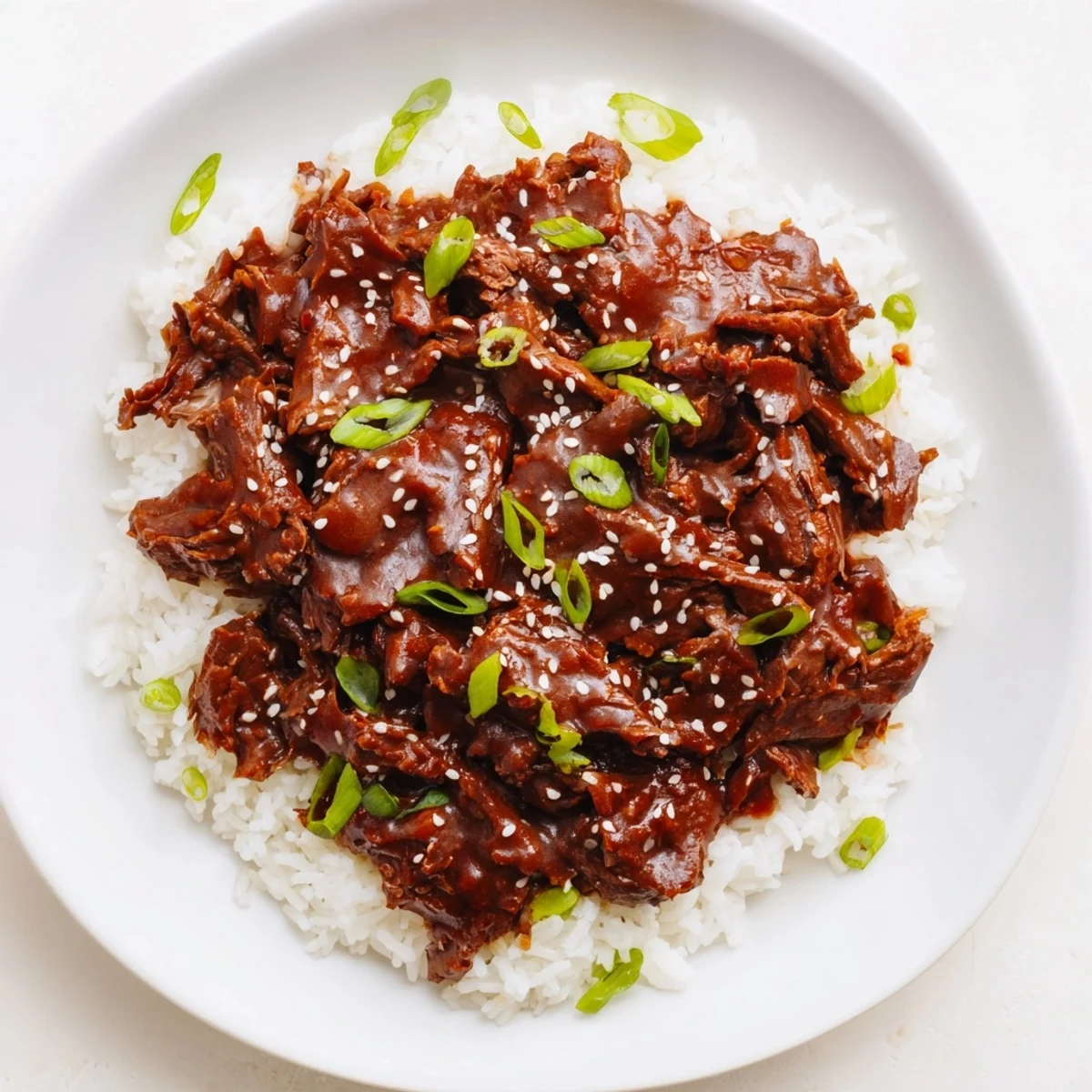 Hearty Crock Pot Korean Beef served in a white bowl over rice, with a savory-sweet sauce that looks rich and glossy.