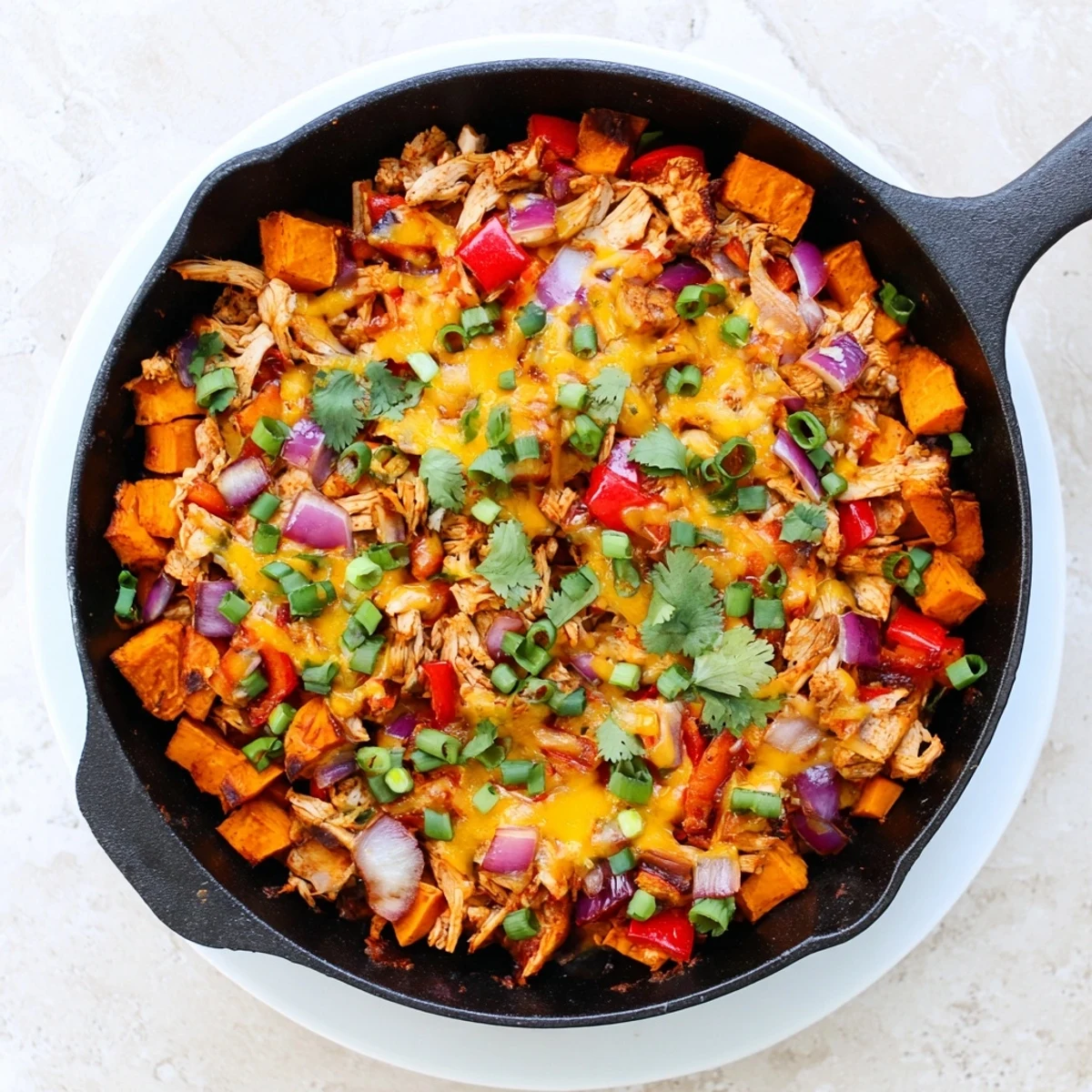 Golden melted cheddar and mozzarella cheese blankets BBQ chicken nestled in a skillet of tender roasted sweet potatoes, topped with green onions.