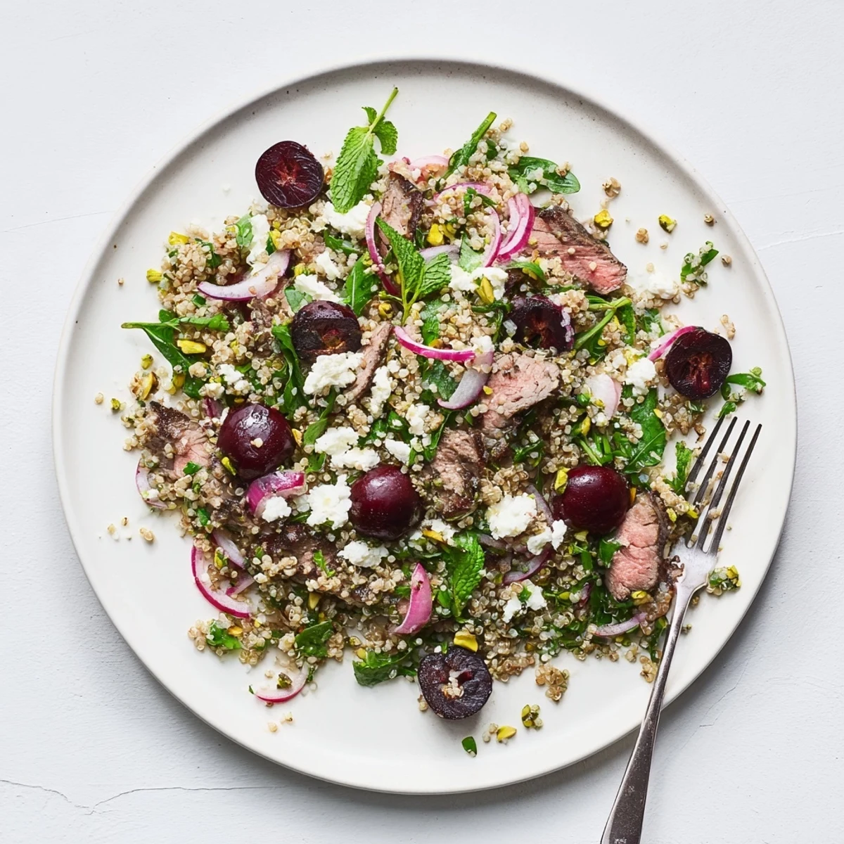 Vibrant cherry quinoa salad with tender spiced lamb fresh herbs and toasted pistachios on a white serving platter