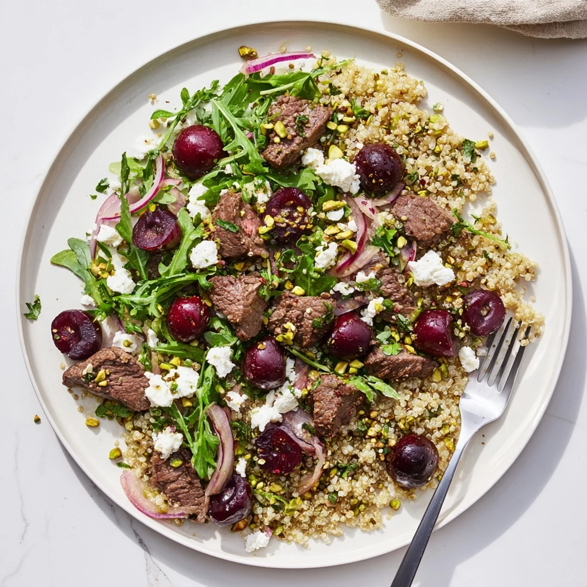 Golden seared lamb strips rest atop fluffy quinoa salad dotted with ruby red cherries and crumbled feta cheese