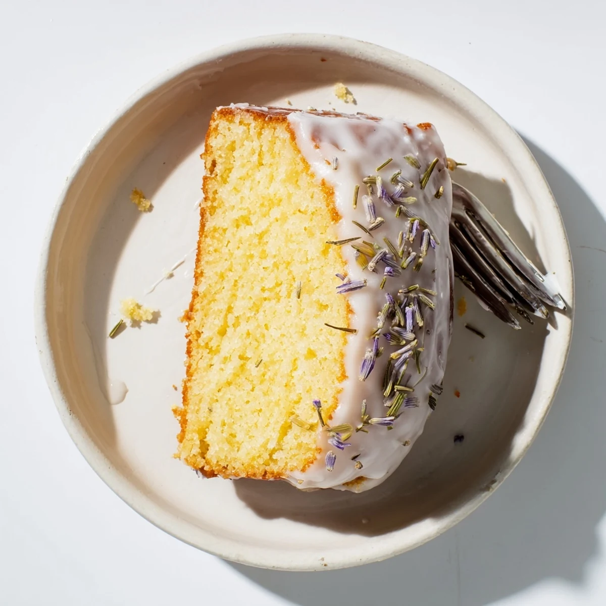 Moist lemon lavender cake slice on a white plate with purple lavender springs