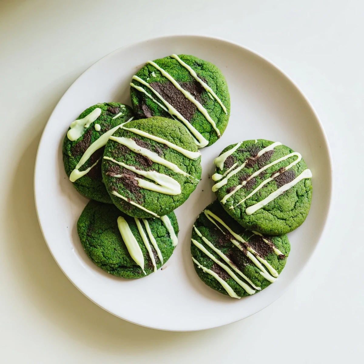 Soft green velvet cookies drizzled with sweet white chocolate on a white plate