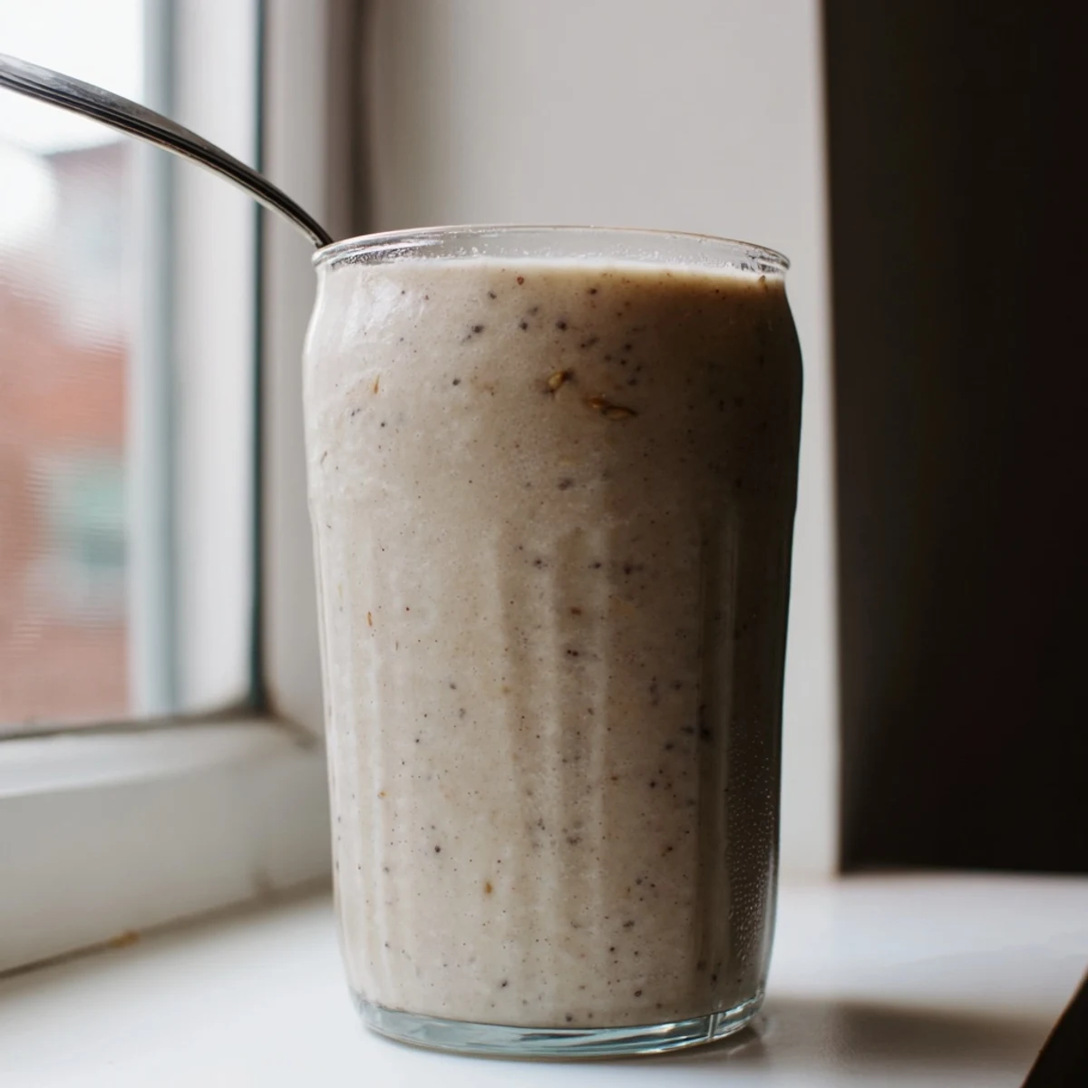 Thick blended Greek yogurt banana smoothie topped with chia seeds and fresh banana slices against a light background
