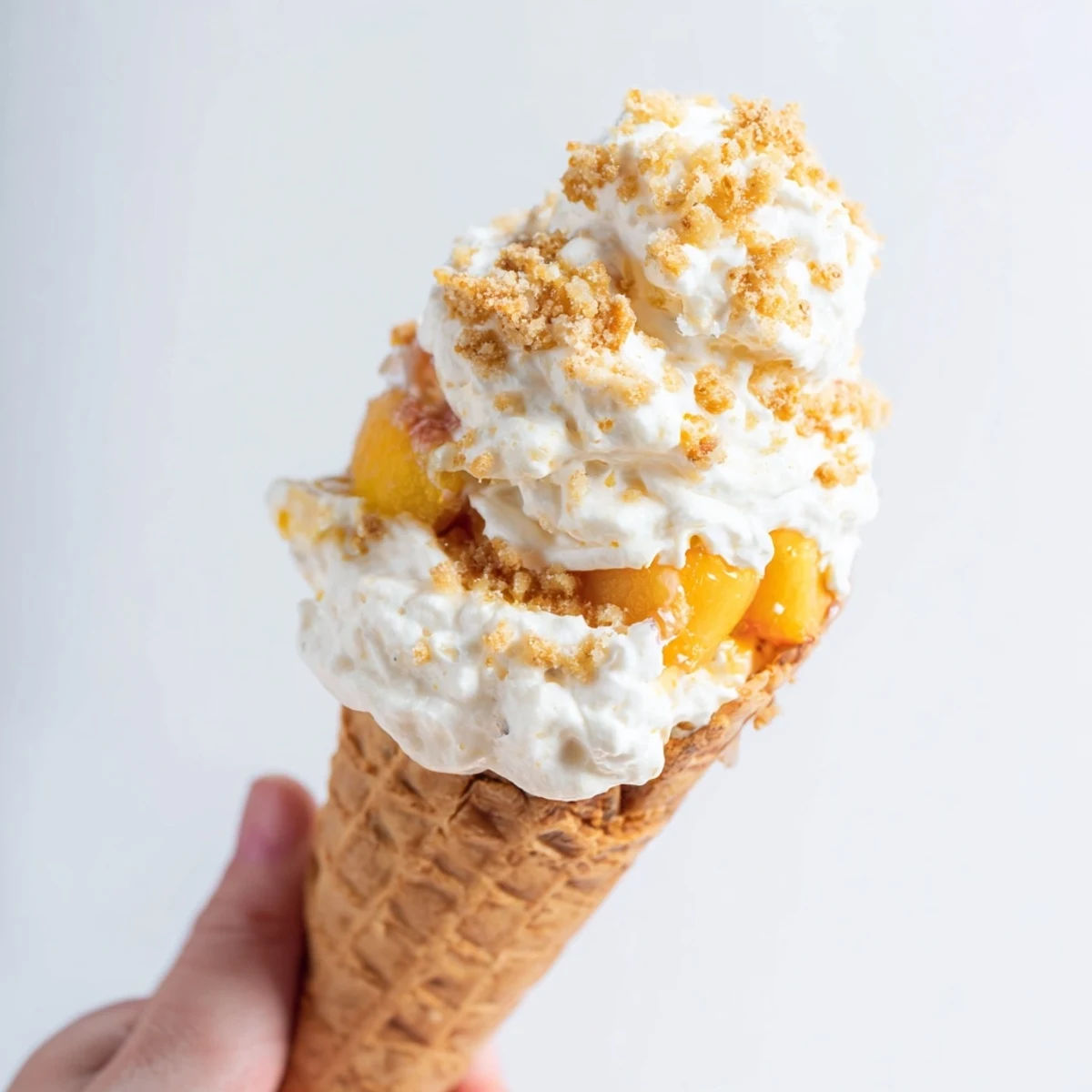Handheld peach cobbler cheesecake cones featuring fresh peaches, fluffy mousse, and buttery crumble