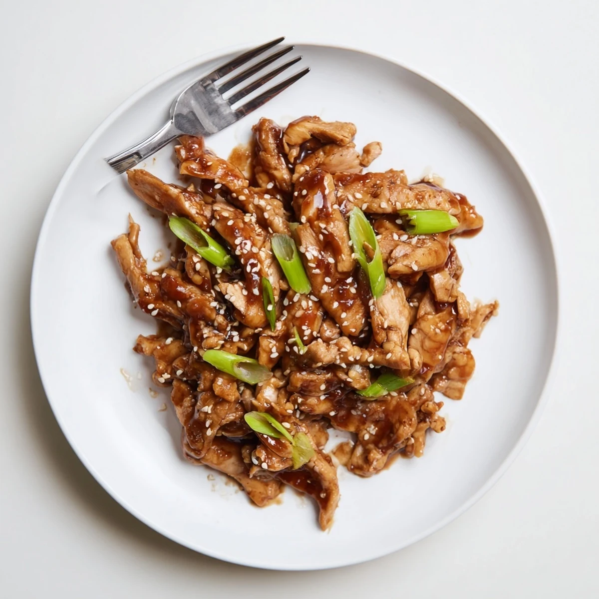 Slow cooker teriyaki chicken glazed in shiny sauce with green onion and sesame garnish