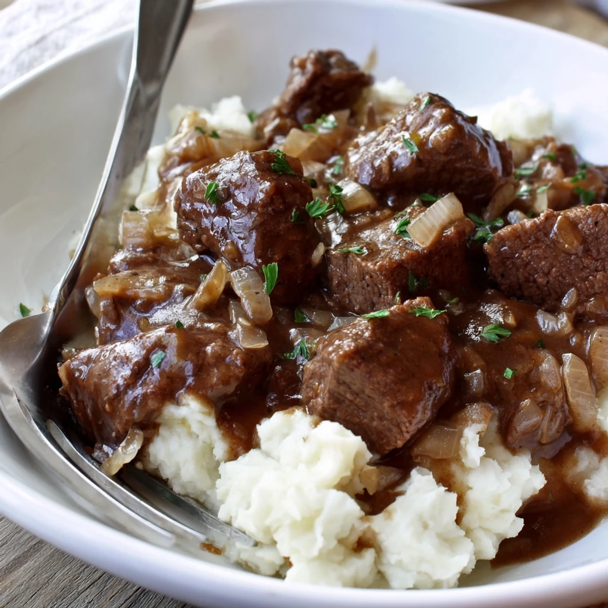 Tender slow cooker beef tips and gravy served over creamy mashed potatoes with fresh parsley garnish