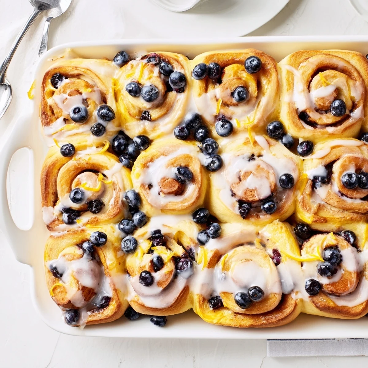 Fresh baked lemon blueberry rolls drizzled with zesty glaze on a serving platter