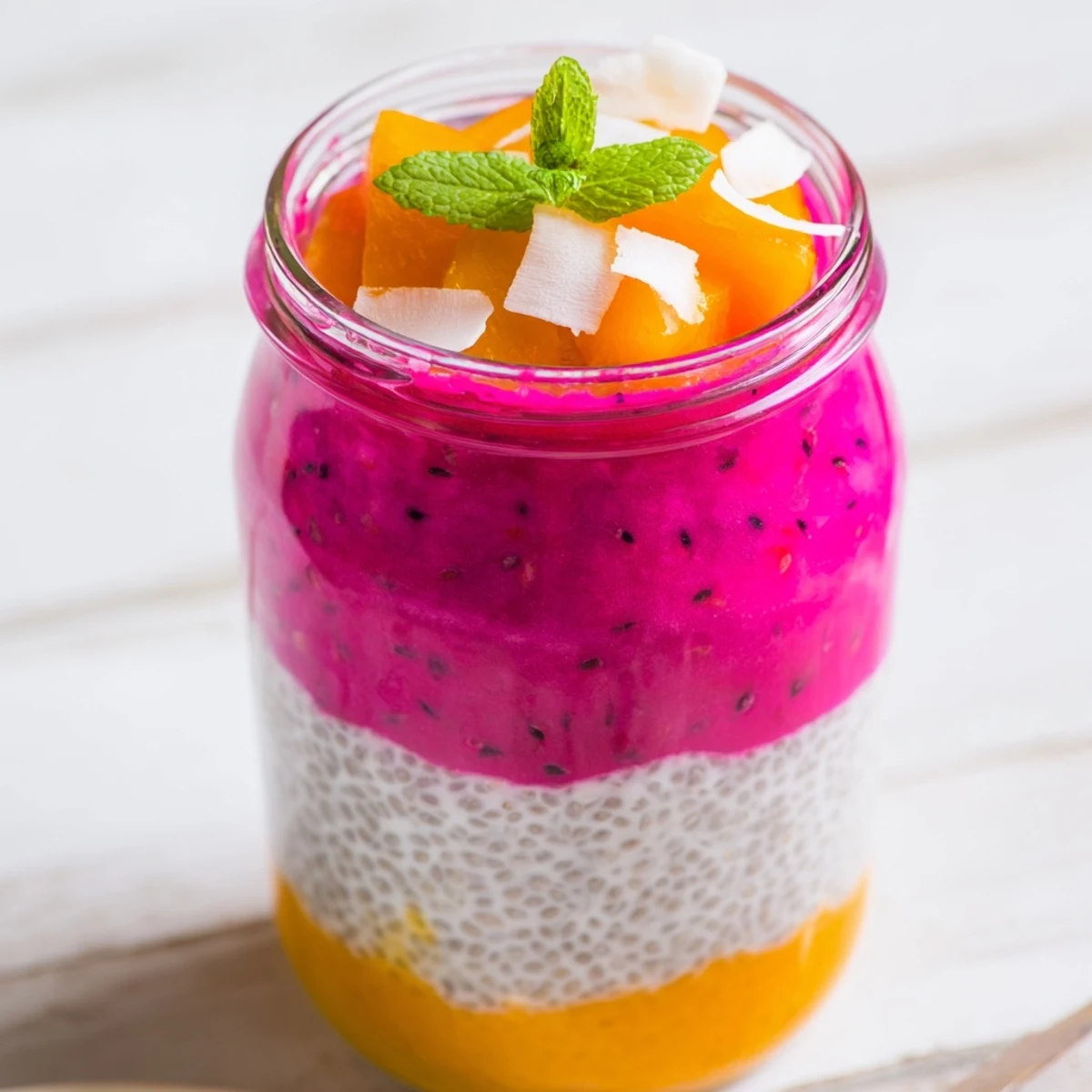 Tropical chia pudding parfait showcasing bright mango and dragon fruit layers with coconut flakes