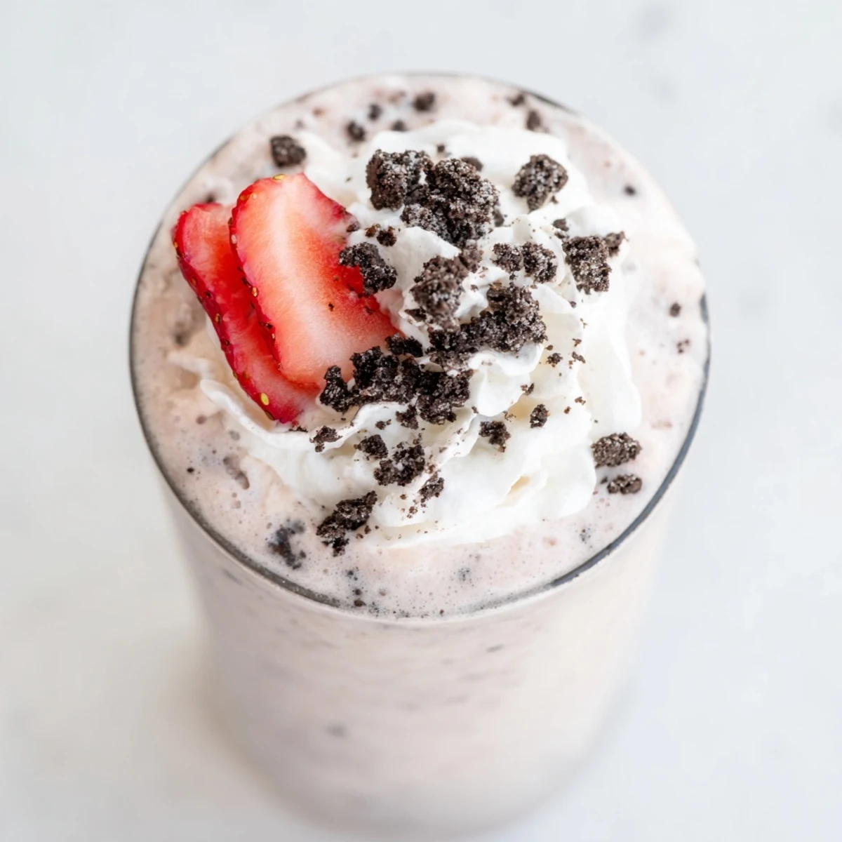 Thick pink strawberry Oreo milkshake topped with whipped cream and crushed cookies in a chilled glass