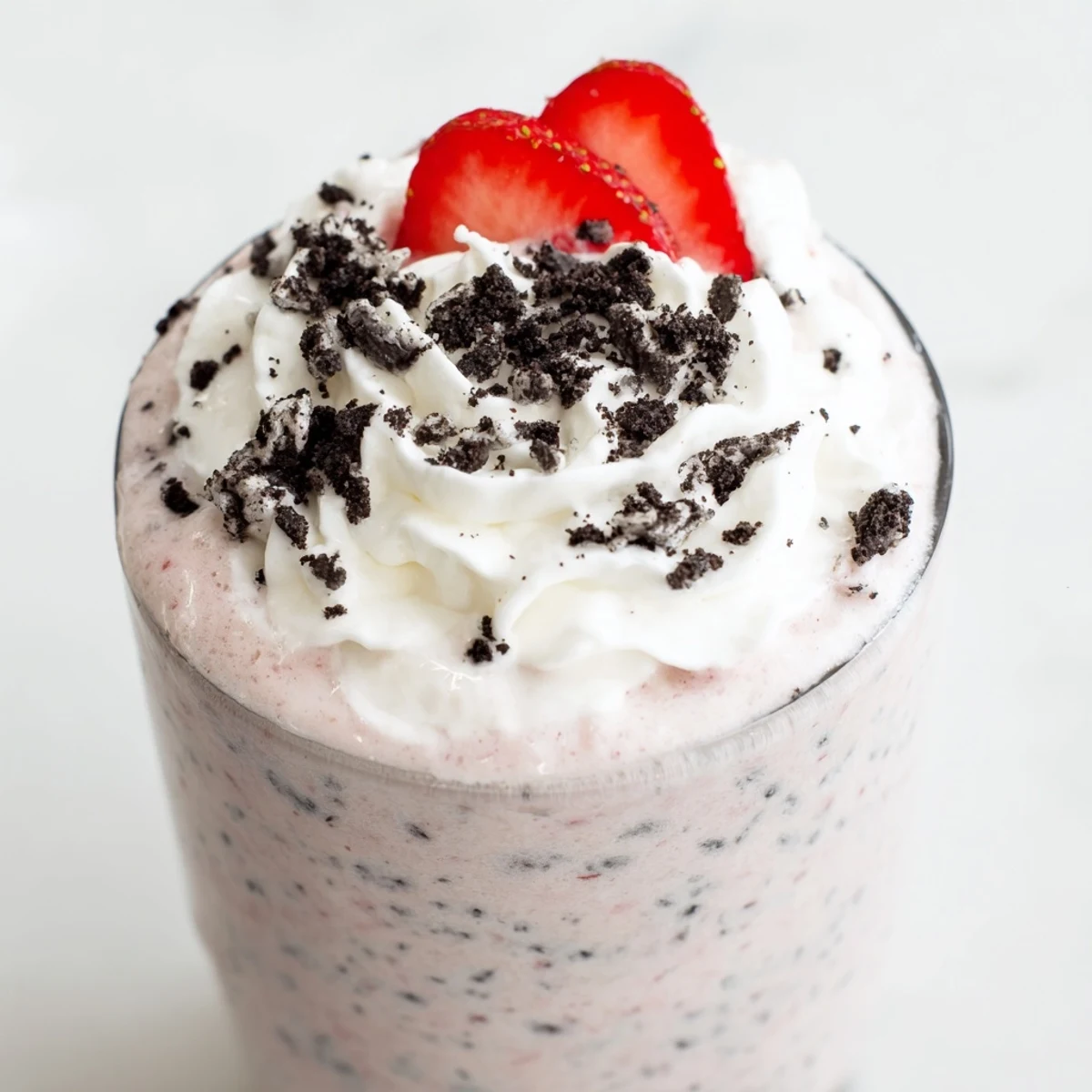 Two tall glasses of pink strawberry Oreo milkshake served with whipped cream and Oreo cookie topping