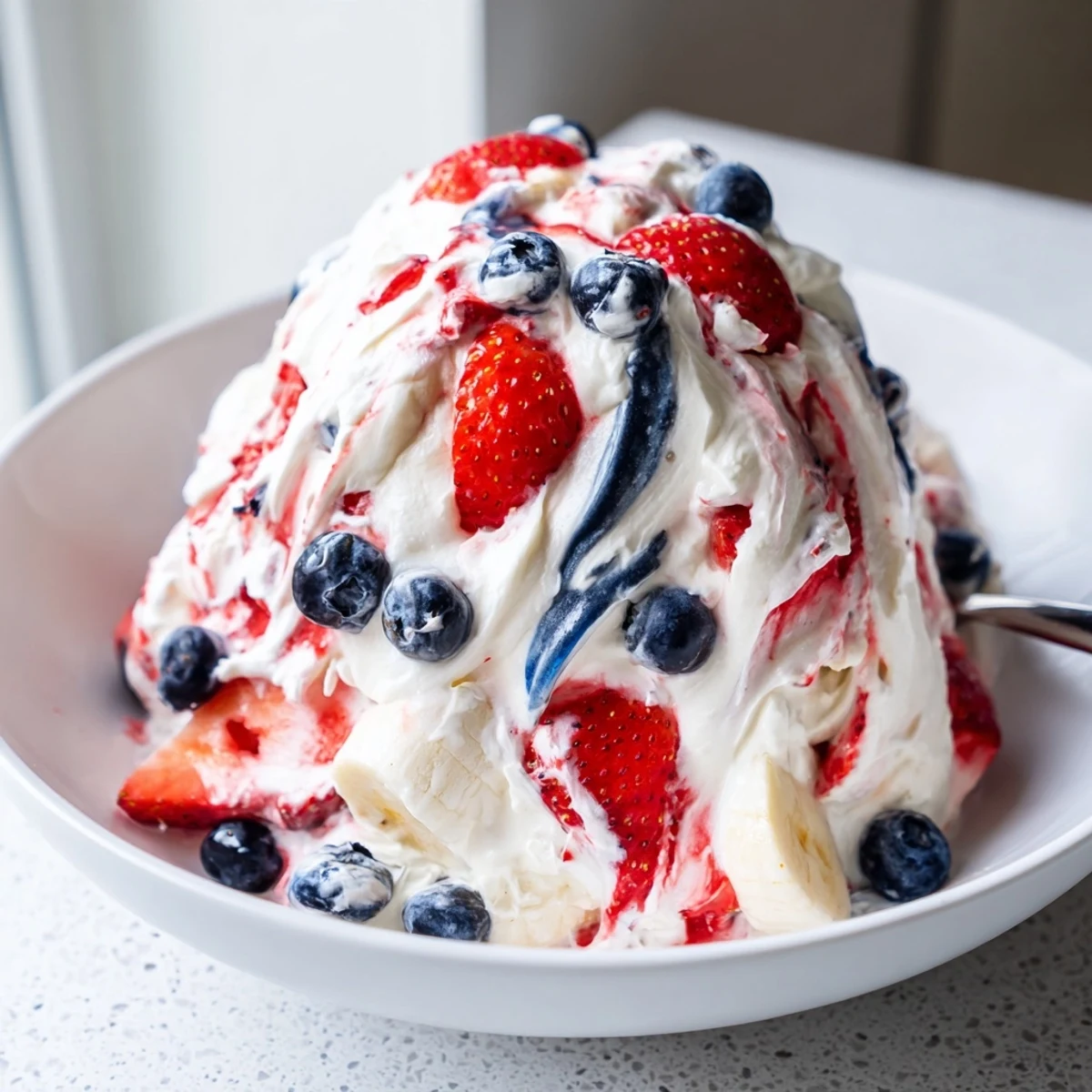 Slice of Red White And Blue Cheesecake Salad topped with extra strawberries, to serve