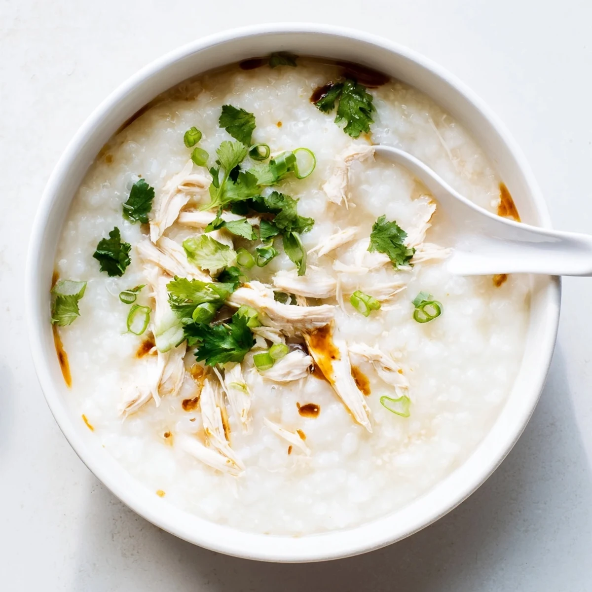 Creamy chicken congee topped with scallions in a white bowl