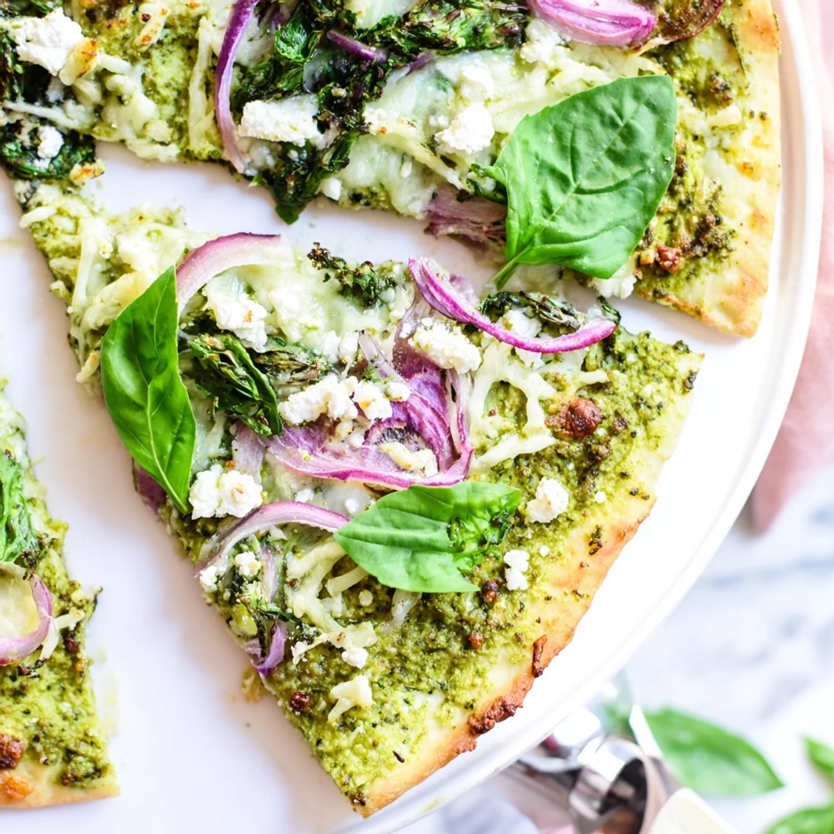 Golden crust pizza spread with creamy broccoli pesto and layered with red onion and greens