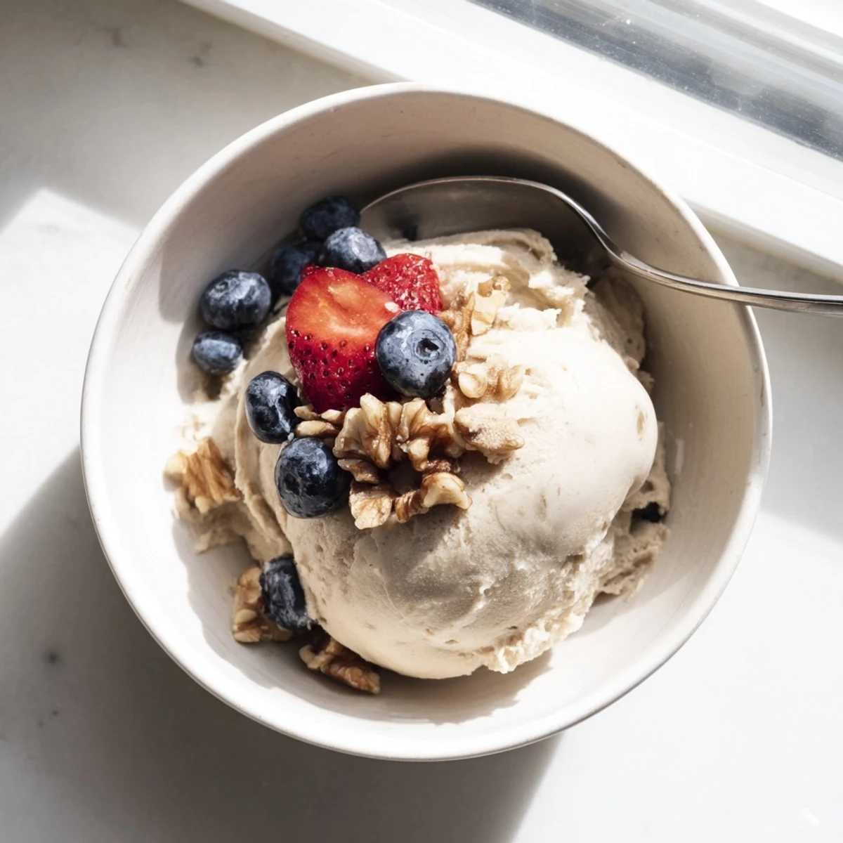 Creamy banana nice cream served in a bowl topped with fresh berries and chopped nuts