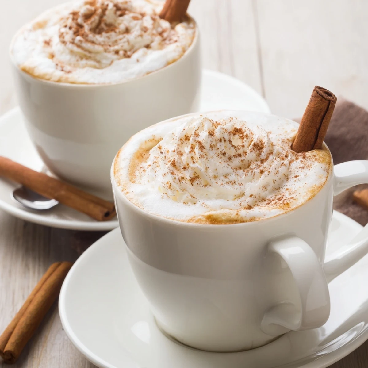 Two steaming Cozy Winter Lattes topped with whipped cream and cinnamon dusting
