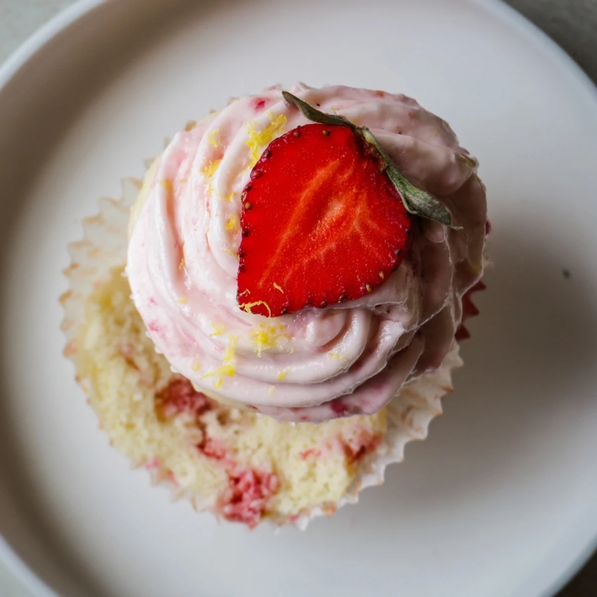 Strawberry Lemonade Cupcakes topped with pink buttercream and fresh strawberry slices on a white plate