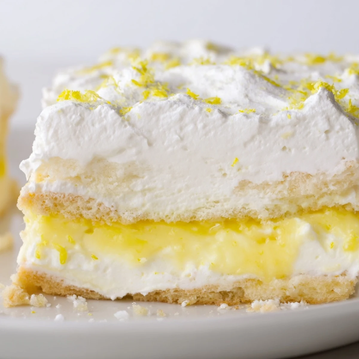 Fresh lemon lush cake on white plate garnished with bright yellow lemon zest